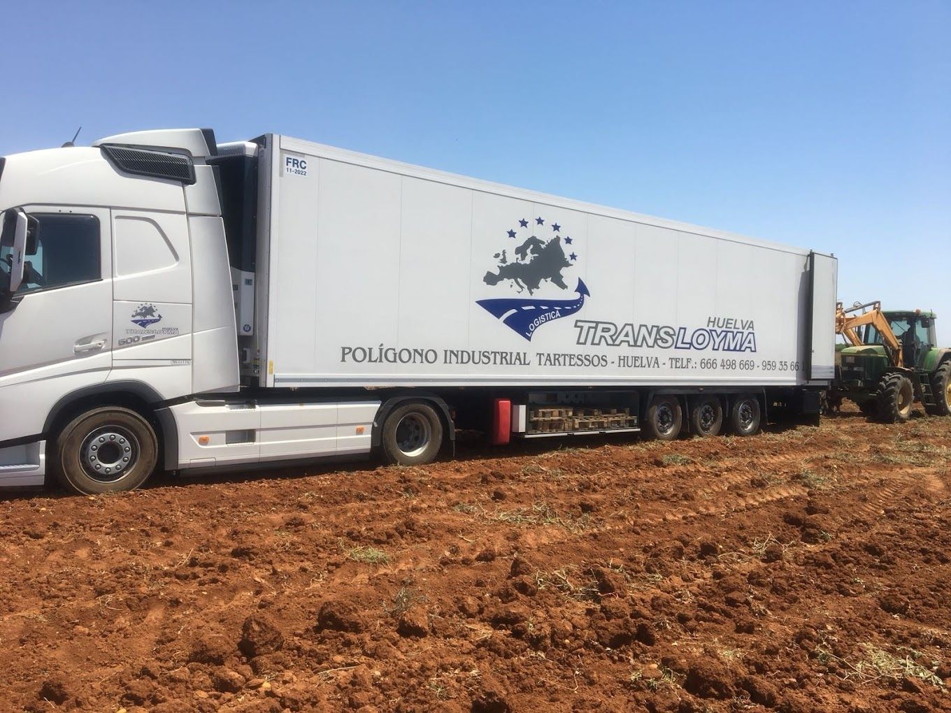 Un camión blanco está estacionado en un campo de tierra al lado de un tractor.