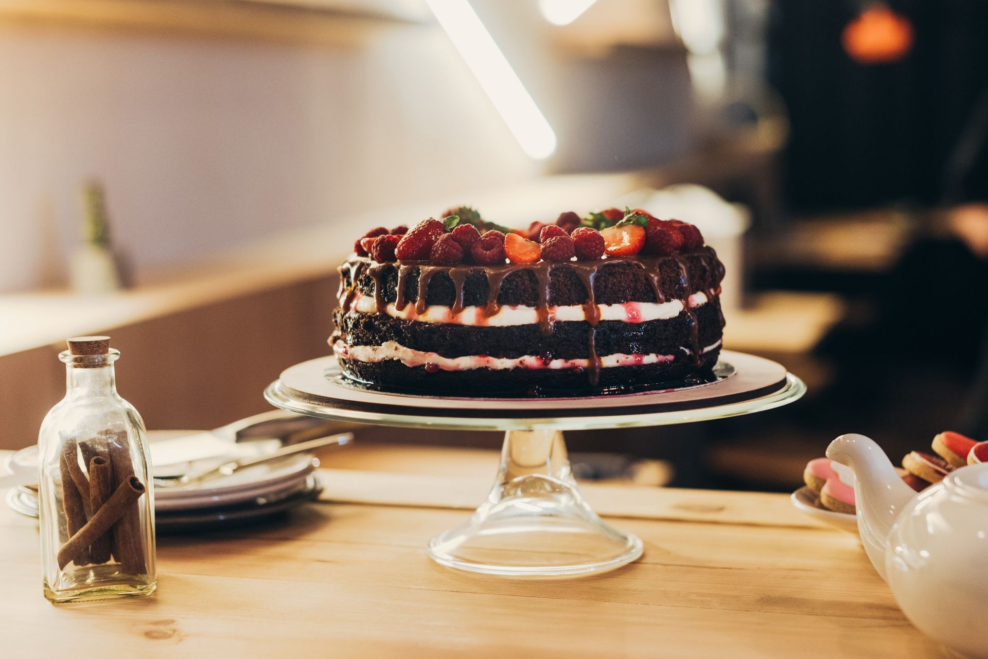 Un pastel de chocolate con frambuesas y crema batida sobre un soporte de vidrio para pasteles sobre una mesa.