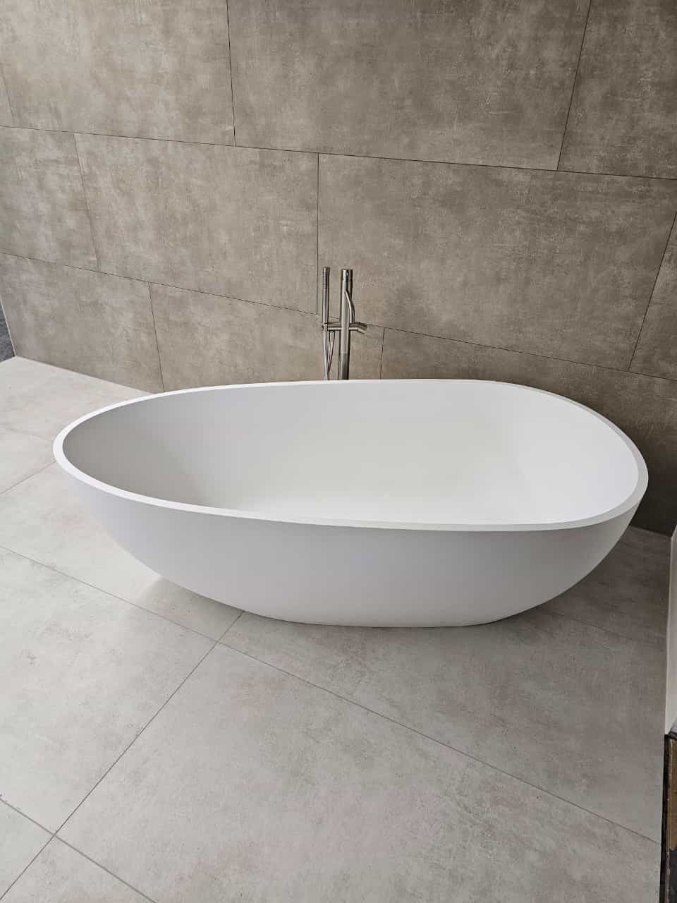 Eine weiße Badewanne steht auf einem gefliesten Boden in einem Badezimmer.