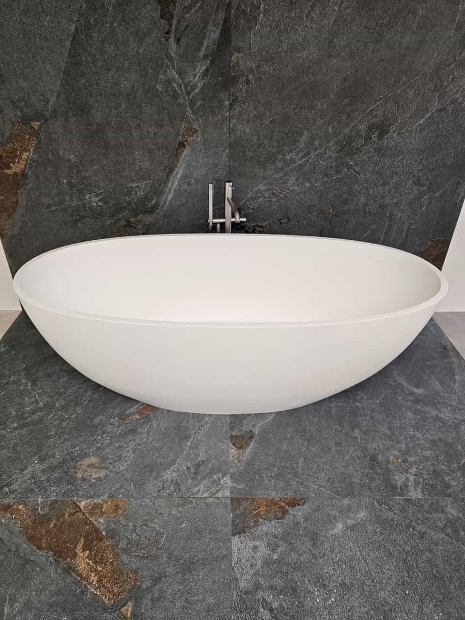 Auf einem schwarz gefliesten Boden steht eine weiße Badewanne.