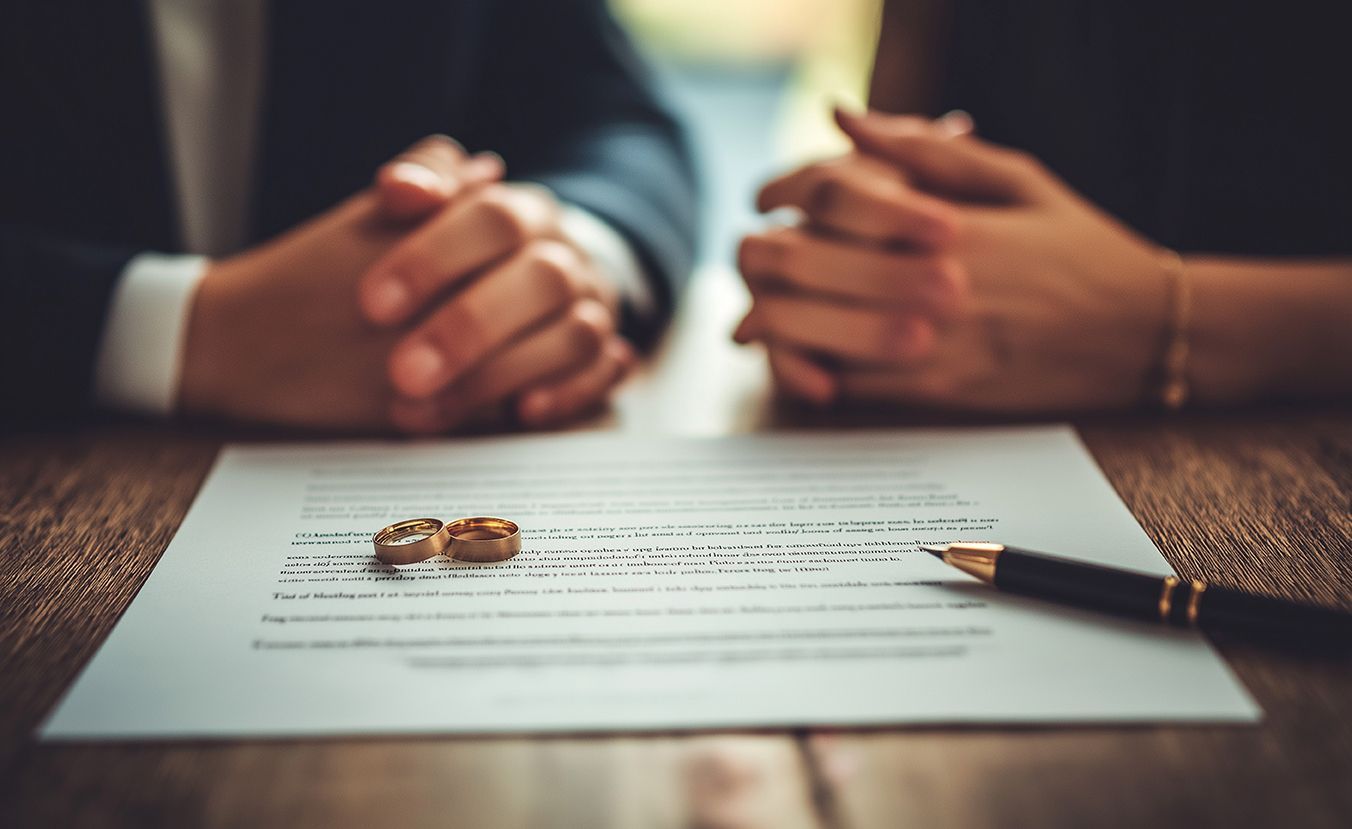 Deux personnes les mains croisées devant un document sur lequel sont posés un stylo et des alliances