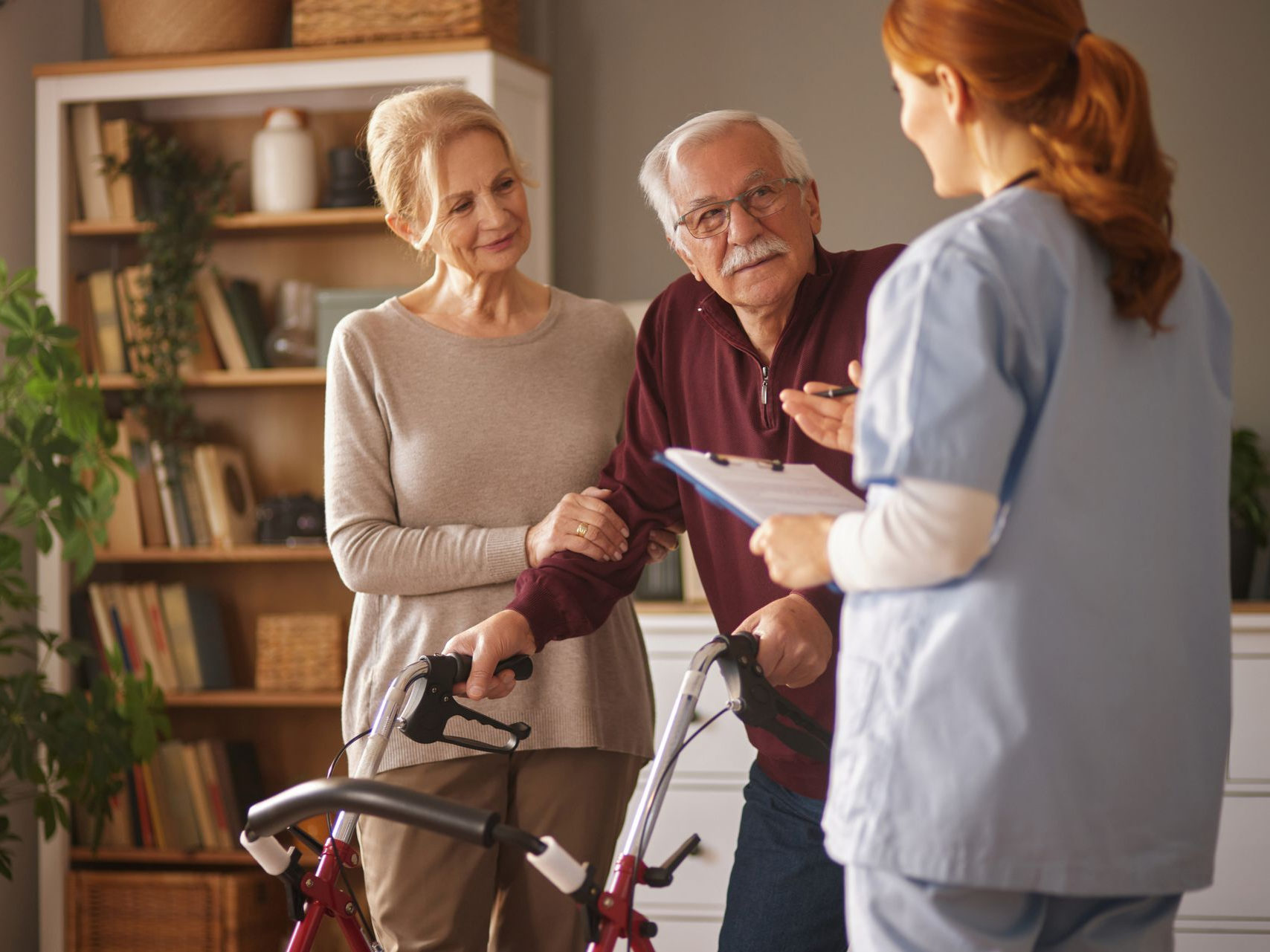 Un couple de personnes âgées avec un déambulateur consulte une infirmière à domicile.