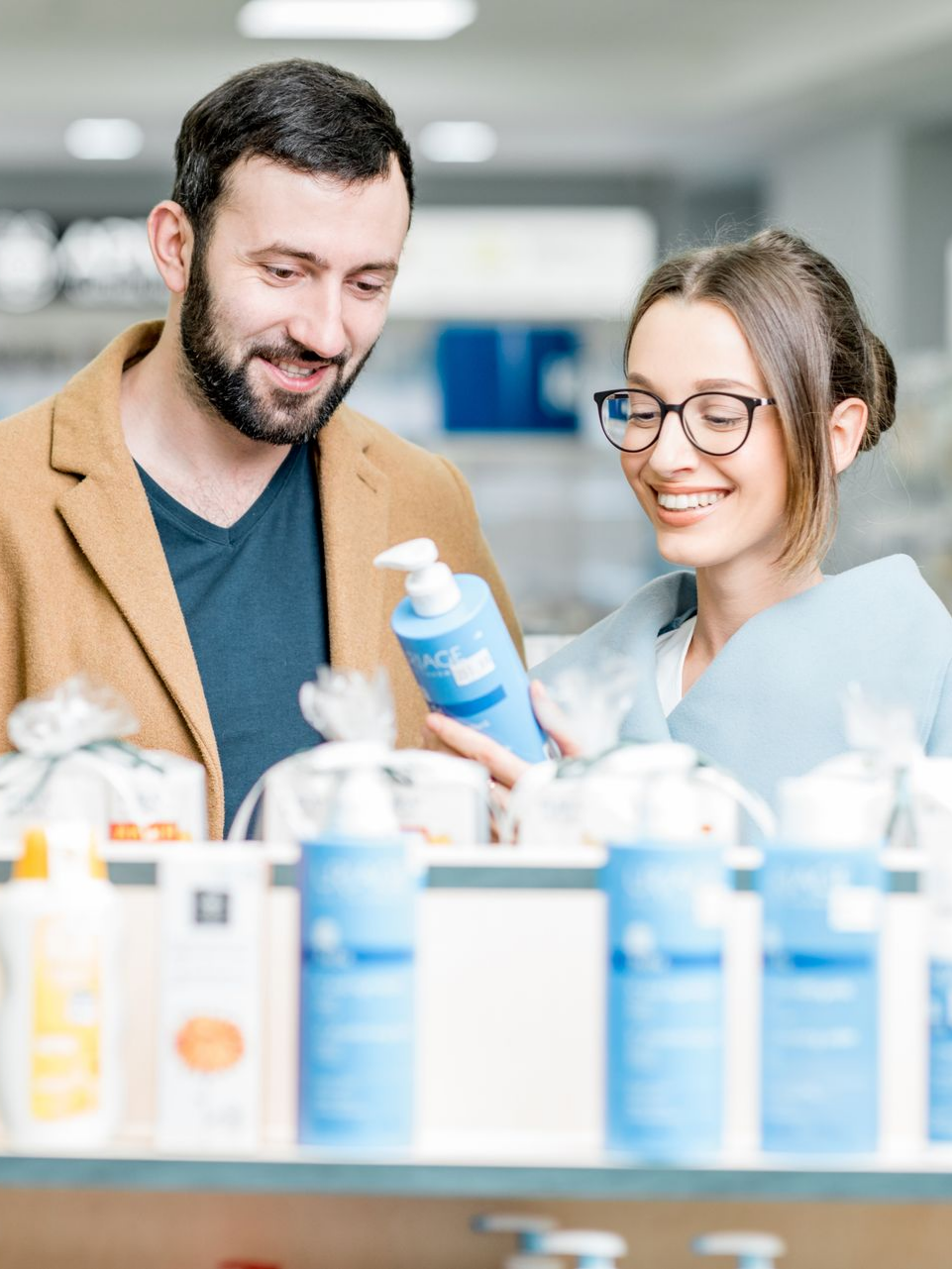 Un homme et une femme examinent un flacon de lotion devant un rayon de pharmacie.