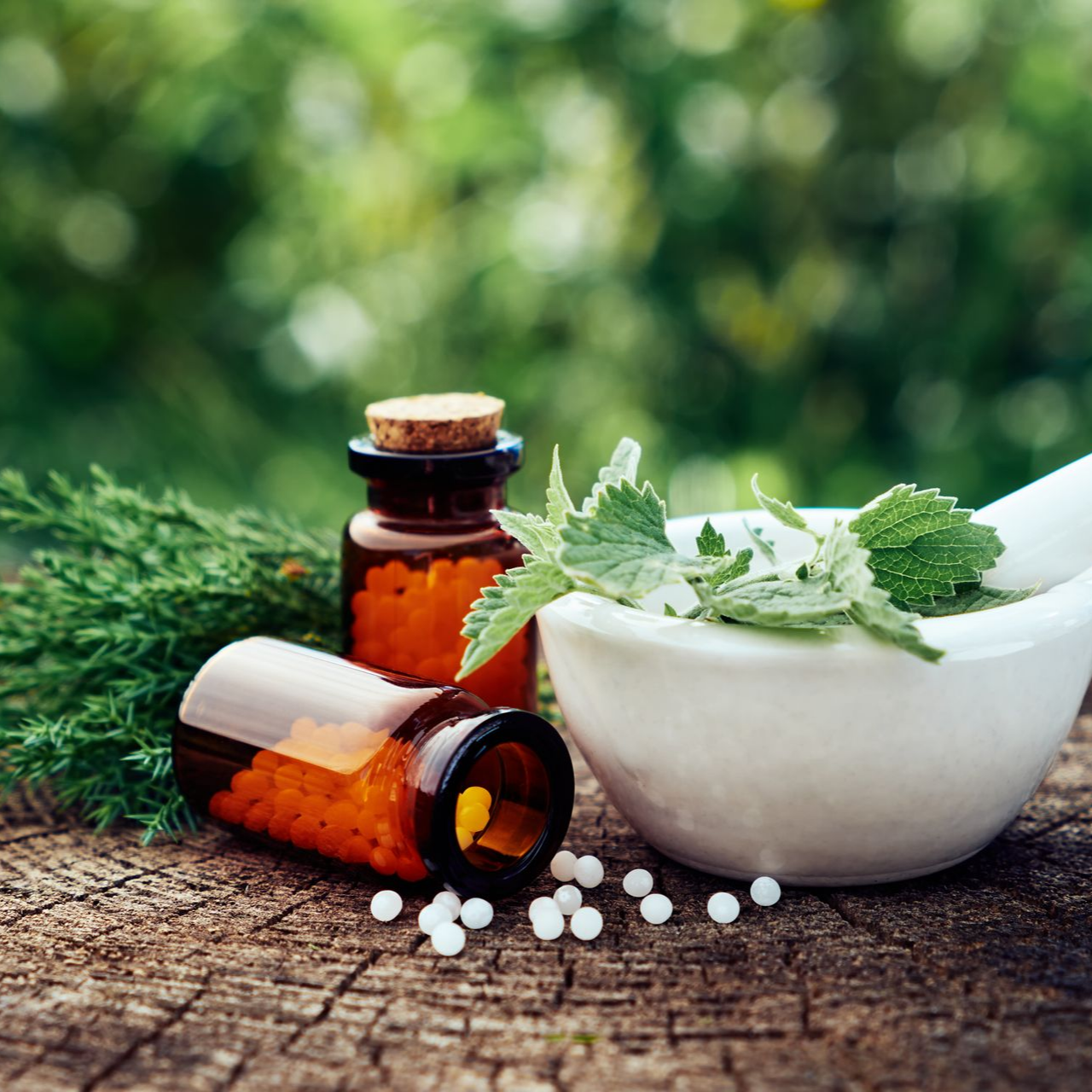 Des petites bouteilles avec des granules d'homéopathie, et un mortier avec un pilon et des herbes médicinales.