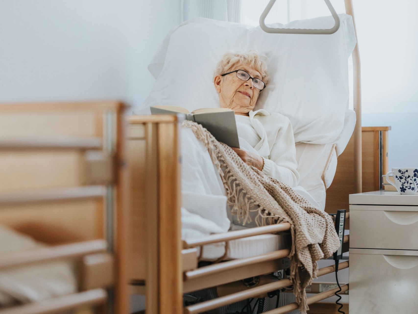 Personne âgée lisant dans son lit médicalisé.