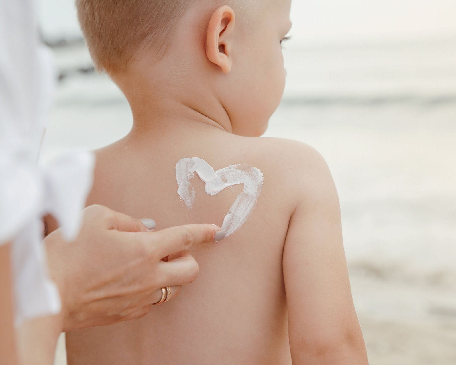 Main appliquant de la crème en forme de cœur sur le dos d'un enfant.