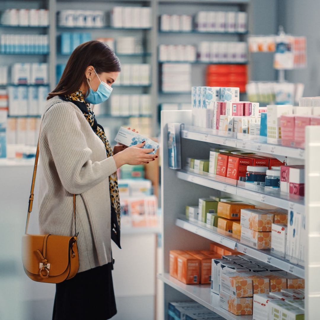 Une femme portant un masque consulte un produit dans les rayons d'une pharmacie.