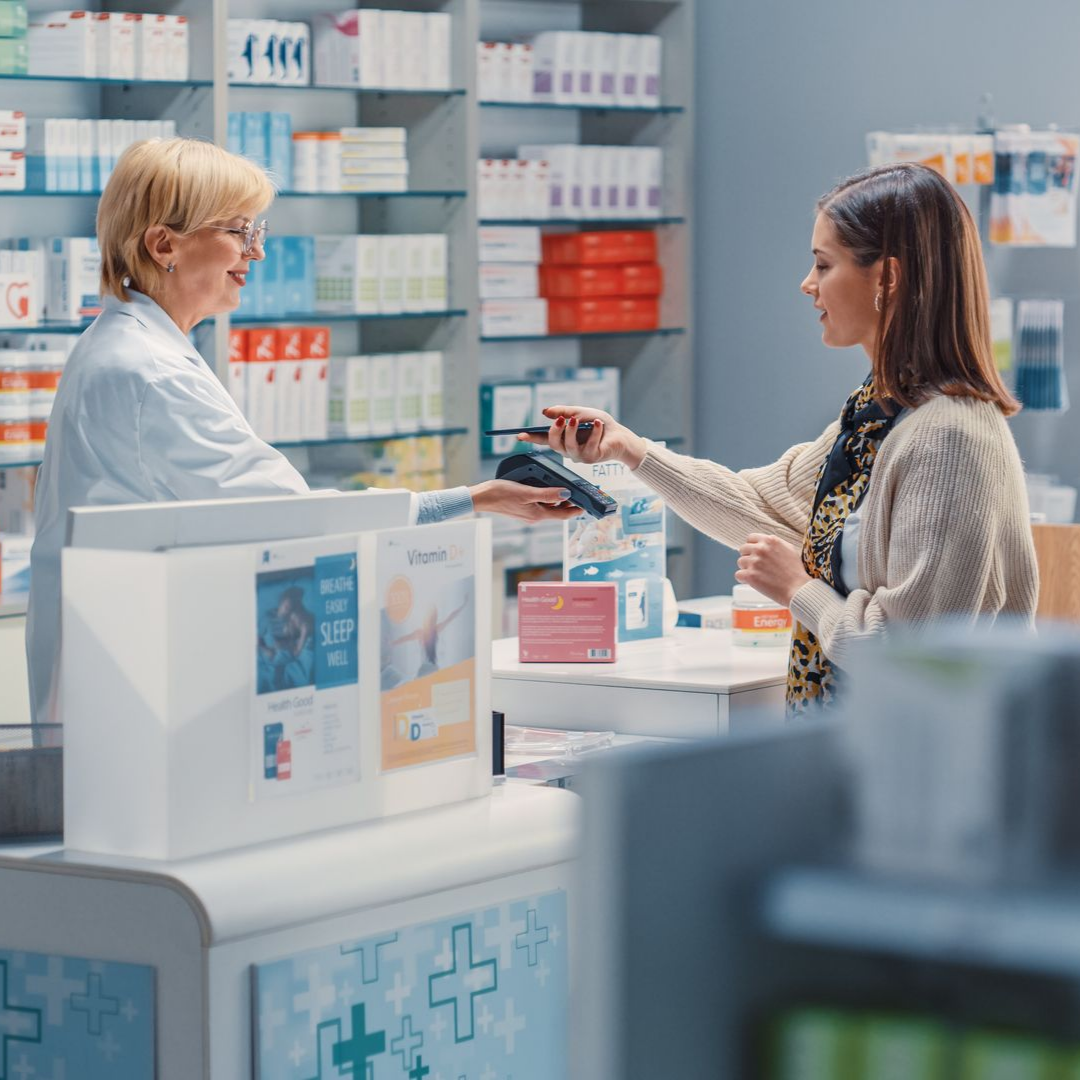 Une pharmacienne tend un terminal bancaire et la cliente règle ses médicaments avec sa carte.