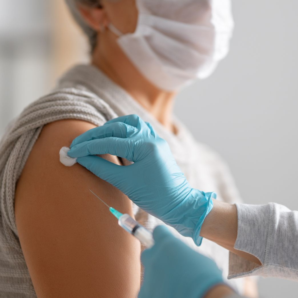 Une personne portant un masque reçoit une injection dans le bras, administrée par une personne portant des gants bleus.