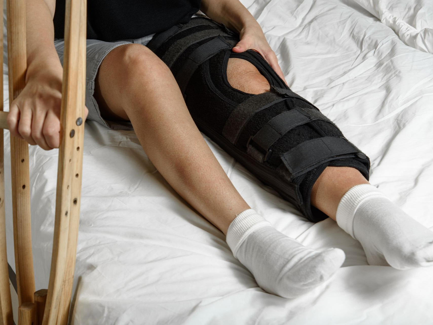 Une personne allongée tient une béquille et porte une genouillère.