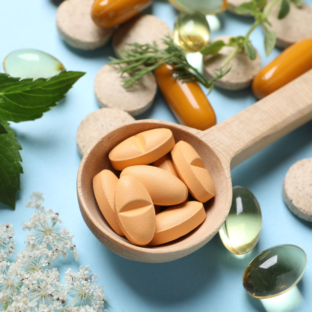 Des comprimés dans une cuillère en bois avec des plantes médicinales et autres médicaments autour.
