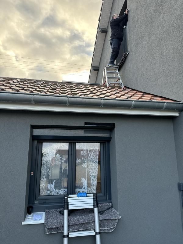 Homme sur un toit en train de fixer des volets roulants à une fenêtre