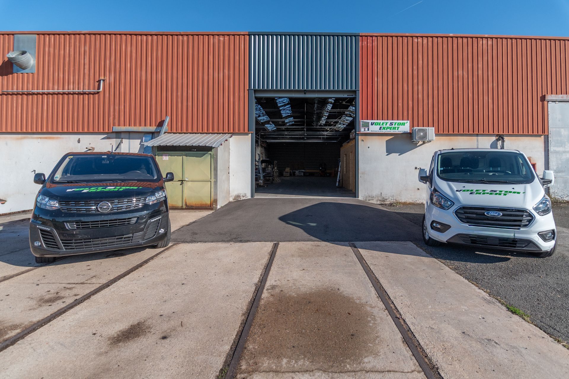 Deux camionnettes d'entreprise stationnées devant l'entrée d'un entrepôt avec un quai de chargement.