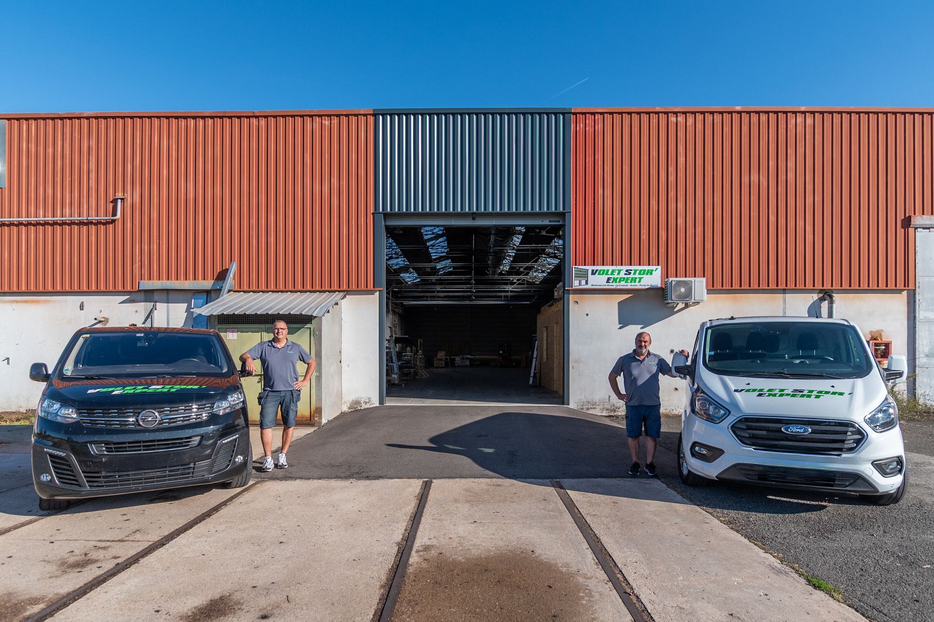 Deux hommes se tiennent près des camionnettes de l'entreprise devant un quai de chargement.