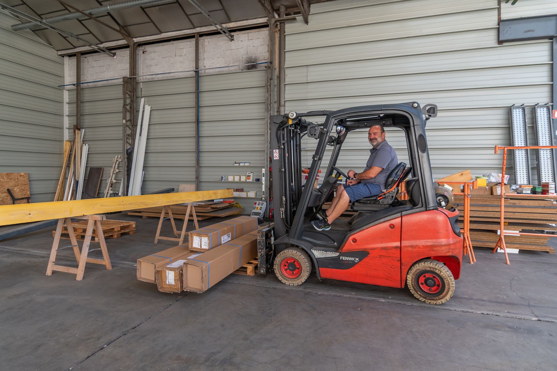 Un homme conduisant un chariot élévateur rouge à l'intérieur d'un entrepôt, déplaçant des matériaux emballés.
