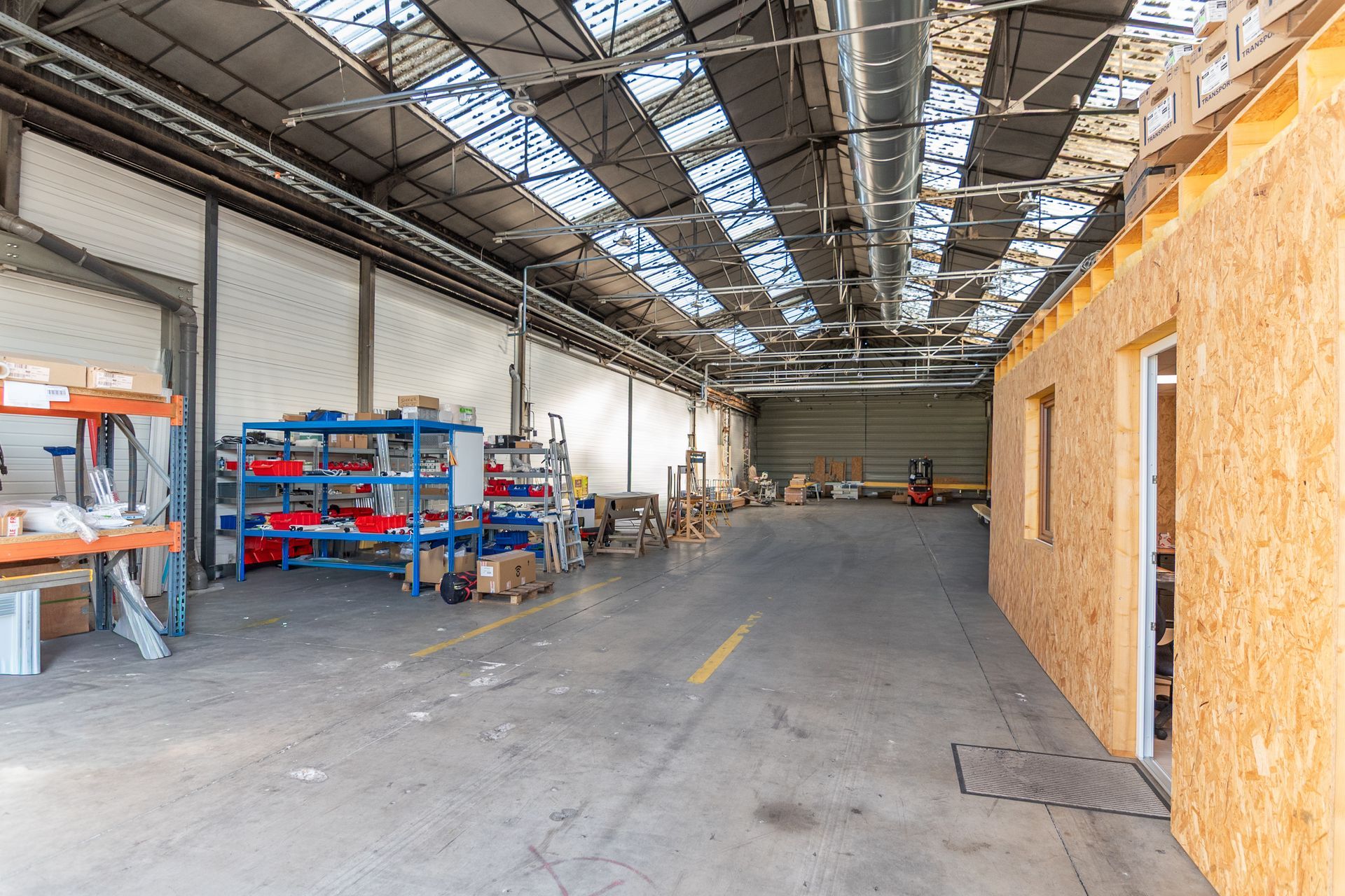 Intérieur d'entrepôt avec étagères, sol en béton et mur à ossature bois. 