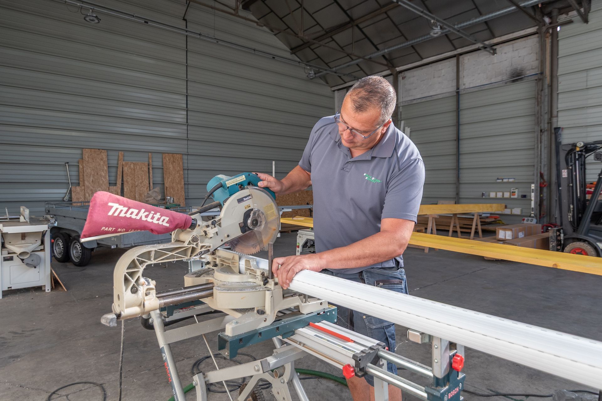 Un homme utilise une scie à onglet pour couper un tuyau blanc dans un atelier.