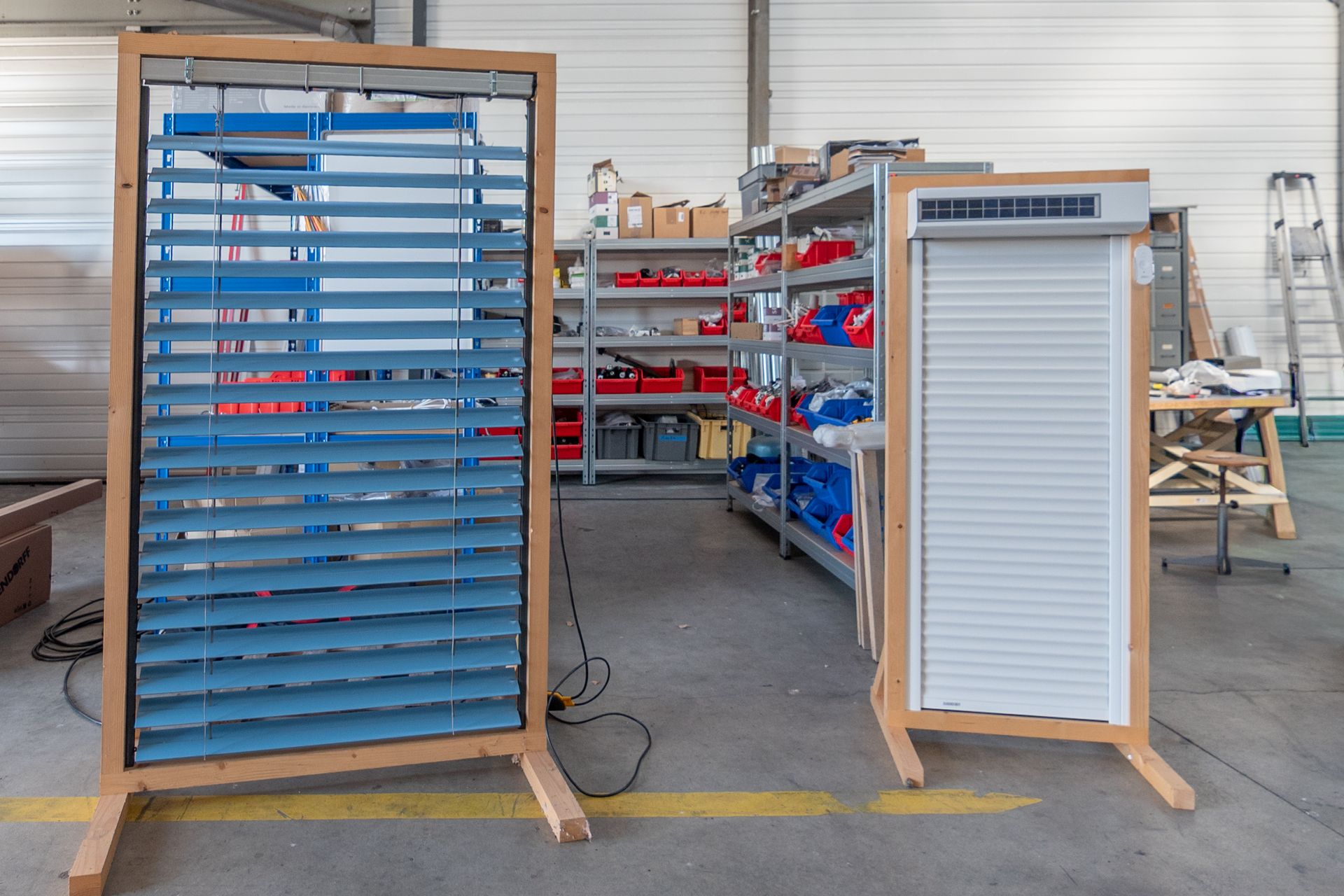 Deux prototypes de stores de fenêtre sur des supports en bois dans un atelier.