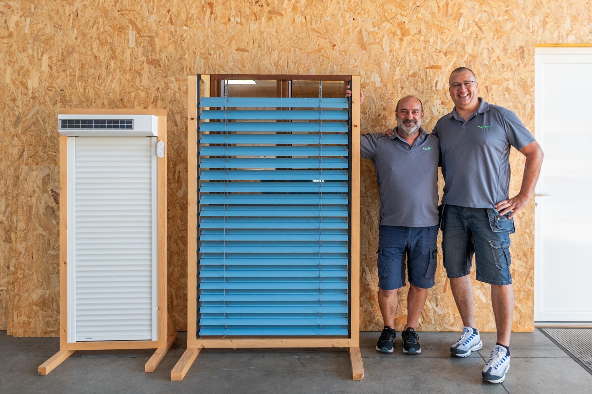 Deux hommes à côté d'un grand modèle de volet bleu et d'un volet  roulant blanc
