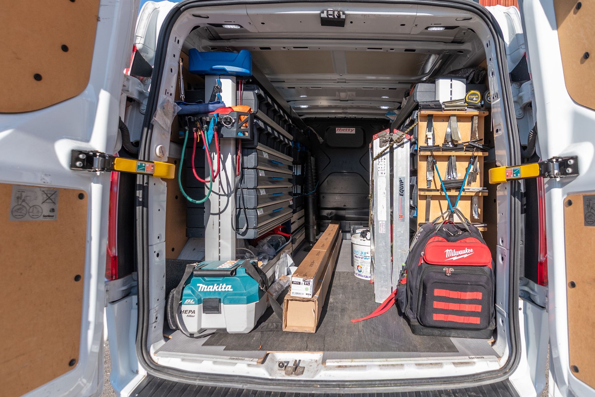 Vue intérieure d'une camionnette blanche, organisée avec des outils et de l'équipement.