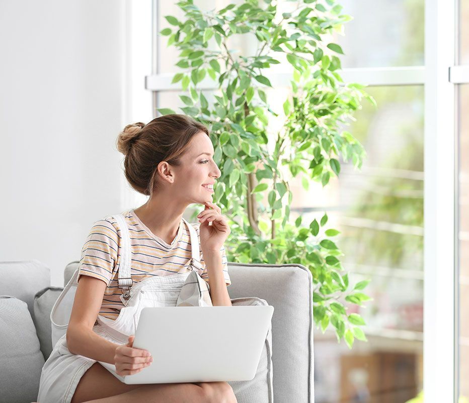 Femme avec un ordinateur sur les genoux qui regarde en direction de sa fenêtre