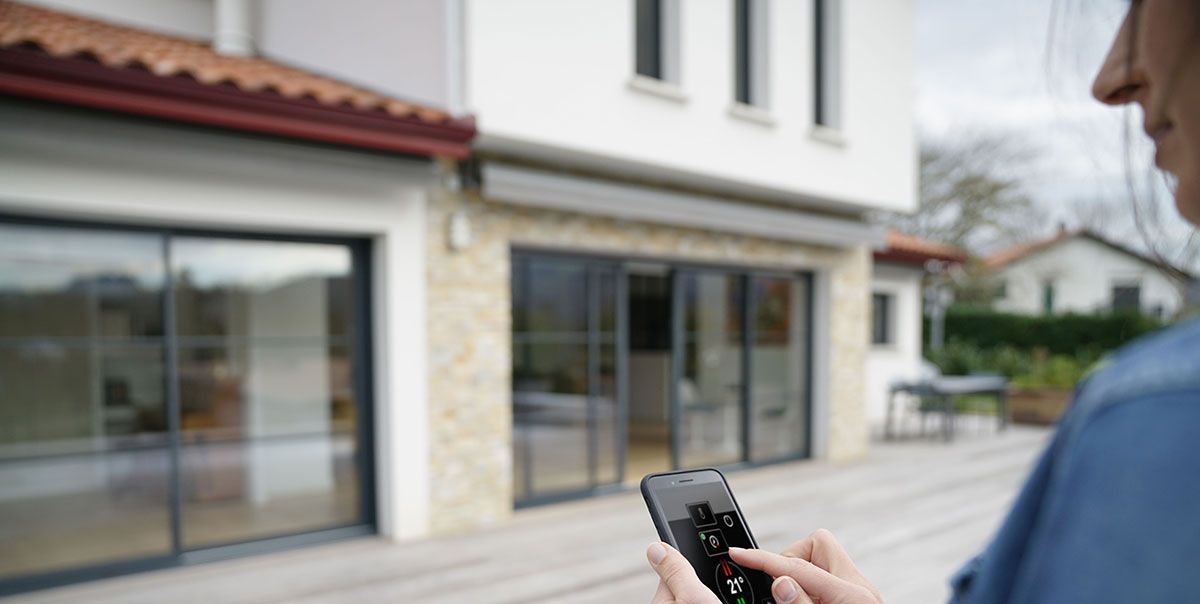 Femme devant sa maison qui contrôle tout le système domotique avec son Smartphone