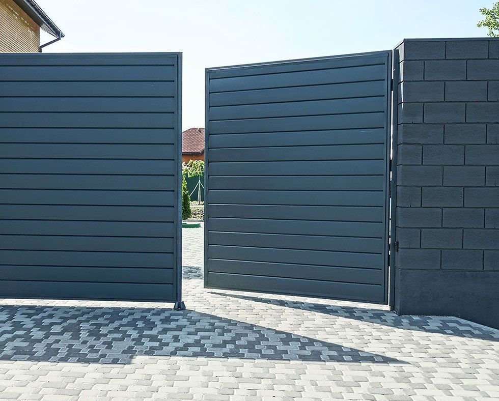 Une porte ouverte en métal noir et une partie d'un mur de briques d'une clôture dans la rue sur un trottoir gris