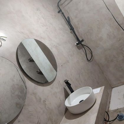 Rincón de baño con espejos redondos, ducha de mano mural y lavabo blanco sobre una pared alicatada en color beige.