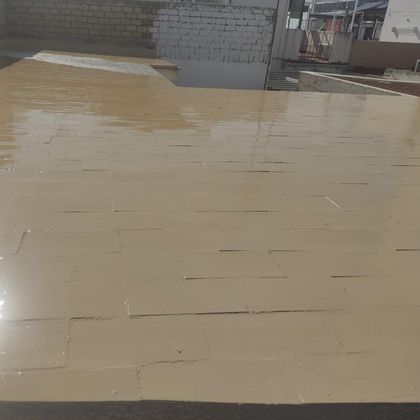 Techo color tostado cubierto con un revestimiento impermeable de color beige, con paredes de ladrillo y un tejado de la ciudad al fondo.