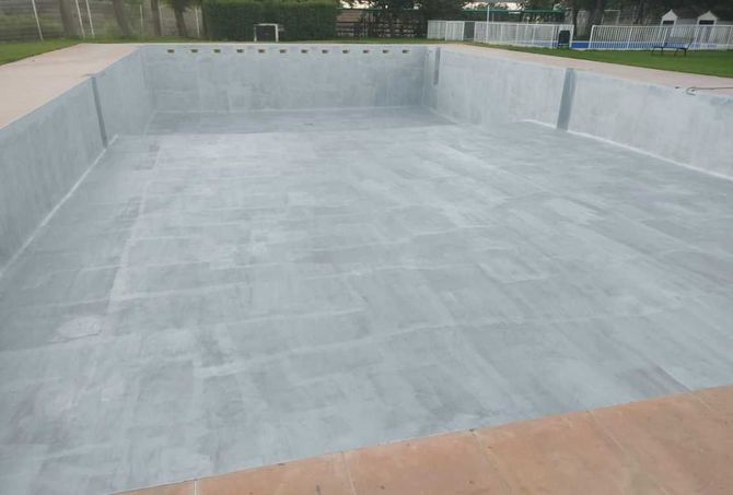 Piscina de hormigón vacía en construcción, con revestimiento de yeso gris y borde color canela.