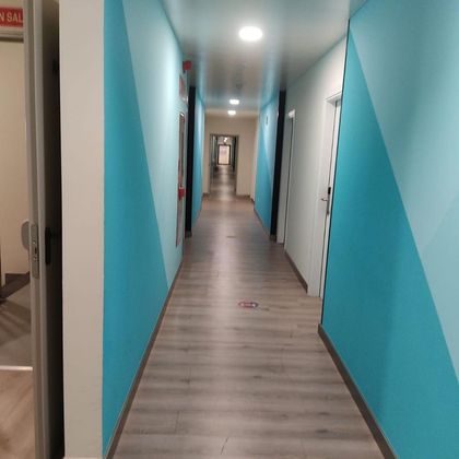 Pasillo largo y estrecho con paredes de color turquesa y blanco, suelo de madera clara y puertas a ambos lados.