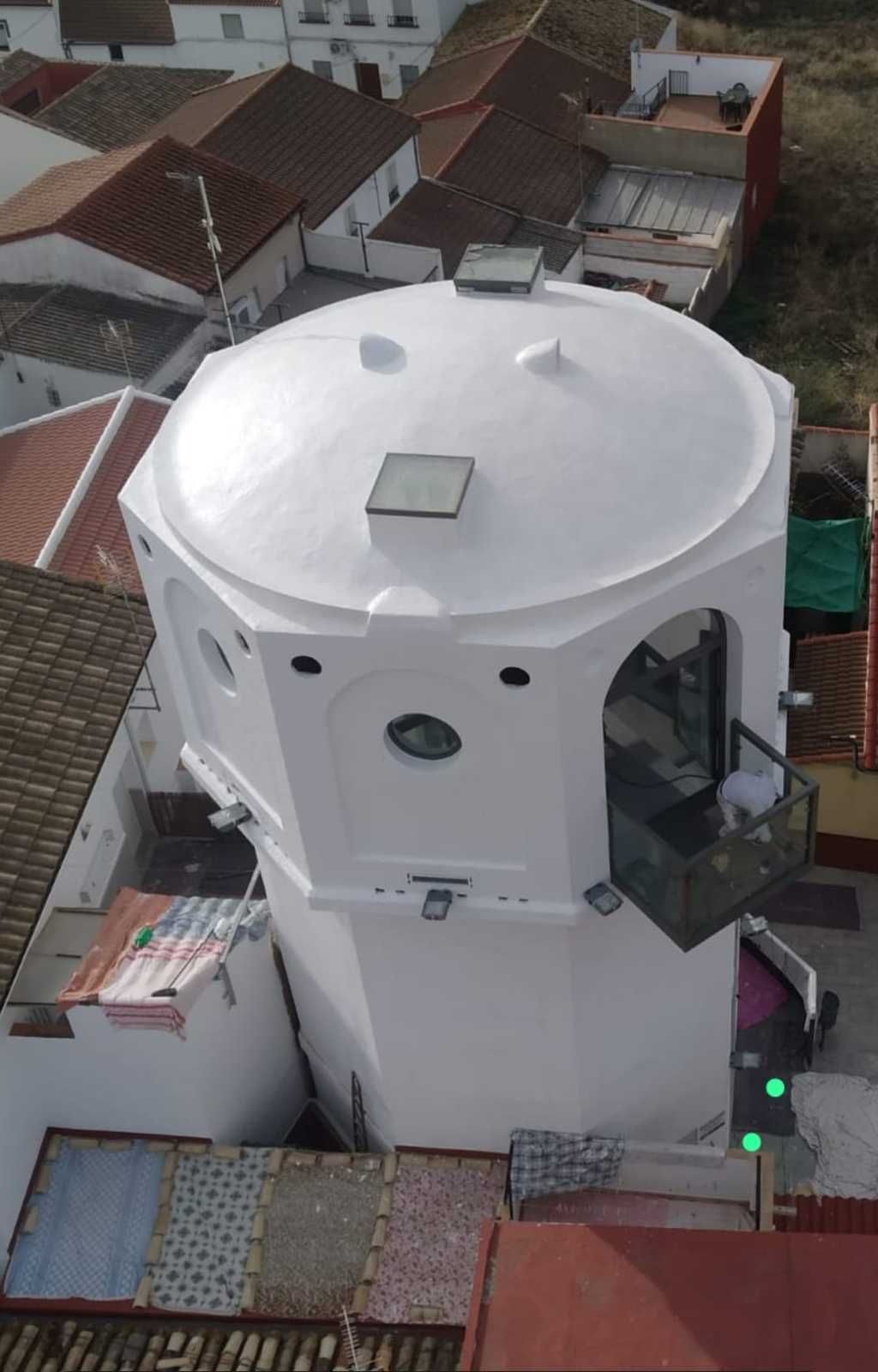 Edificio cilíndrico blanco con techo abovedado, visto desde arriba entre las casas y tejados cercanos.