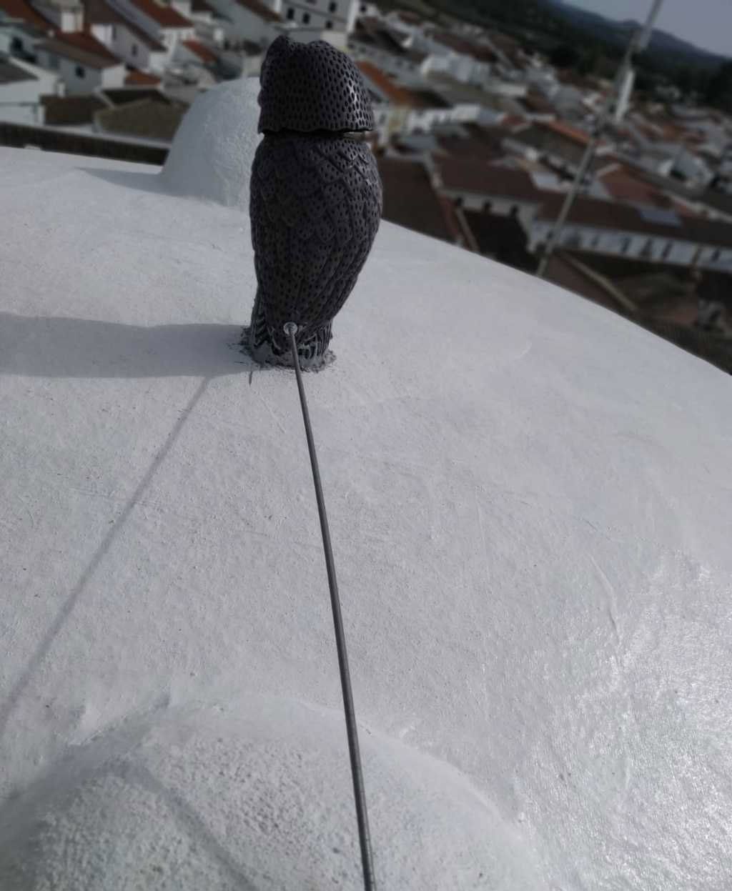 Objeto de punto oscuro sobre una azotea blanca con el perfil de la ciudad de fondo.