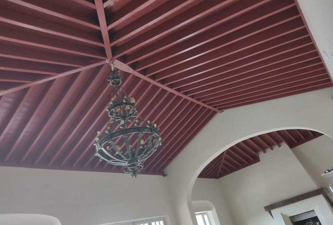 Habitación blanca con techo abovedado rojo y lámpara de araña colgante bajo una abertura arqueada.