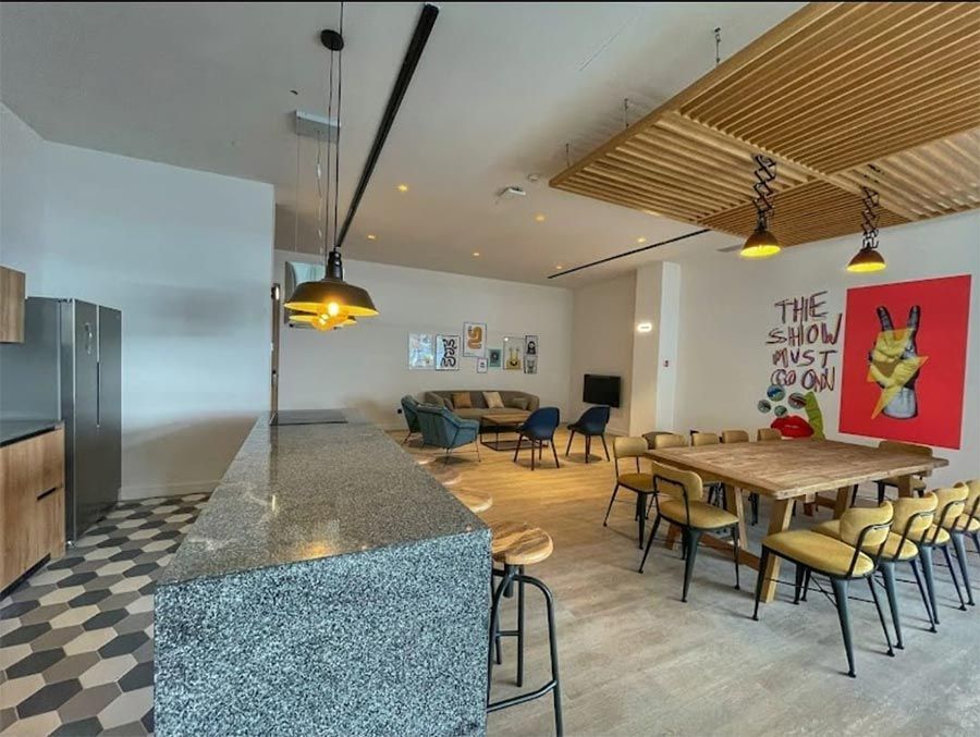 Interior de restaurante moderno con mesas de madera, sillas amarillas, suelo estampado y una larga barra de piedra.