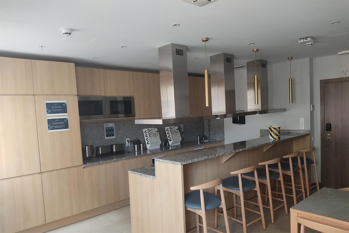 Cocina moderna con armarios de madera clara, isla de granito, taburetes de bar y lámparas colgantes.
