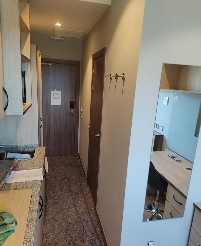 Pasillo estrecho de un apartamento con armarios de madera, percheros, espejo y una puerta al final.