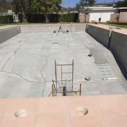 Piscina de hormigón vacía en construcción, con una escalera y andamios en el centro.