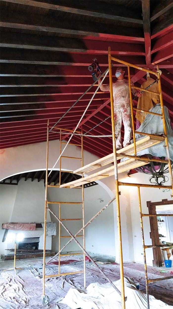 Andamios en el interior de un edificio con un trabajador pintando un techo rojo cerca de una pared curva.