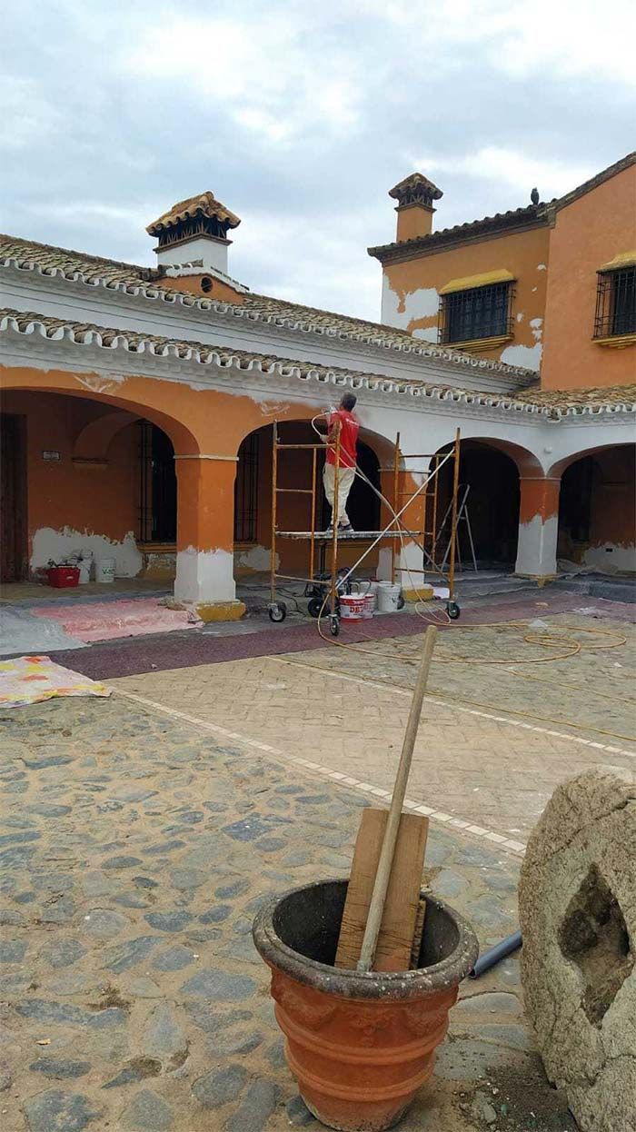 Patio con arcos naranjas, suelo empedrado, una planta en maceta y una escalera bajo un tejado de tejas.