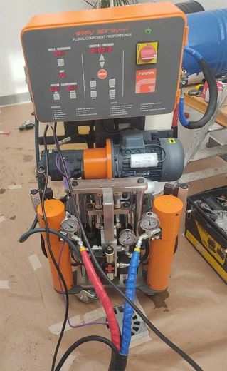 Máquina industrial con componentes, manómetros, mangueras y panel de control de color naranja y negro en un taller.