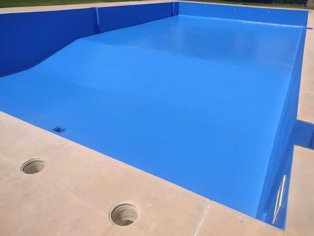 Piscina azul vacía junto a una terraza beige con agujeros de drenaje.