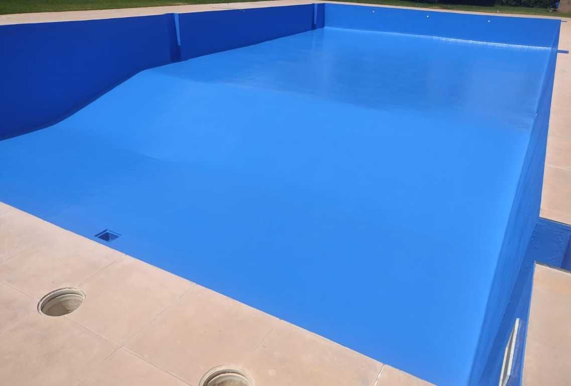 Piscina azul en construcción junto a una terraza beige con agujeros de drenaje.