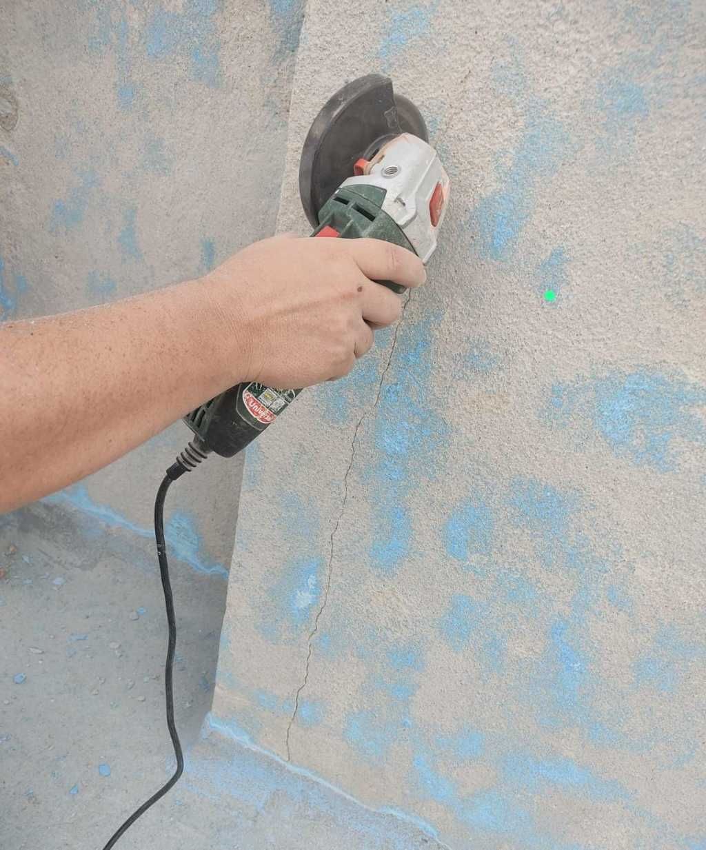 Mano usando una amoladora angular en una pared de hormigón texturizado, creando polvo