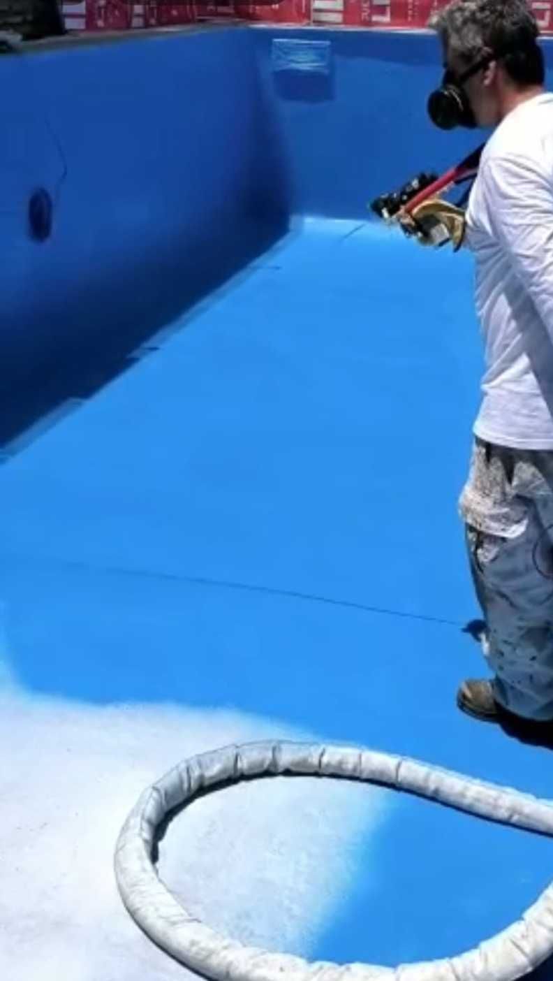 Una persona limpia con agua a presión el interior de una piscina de color azul brillante mientras está de pie en el borde.