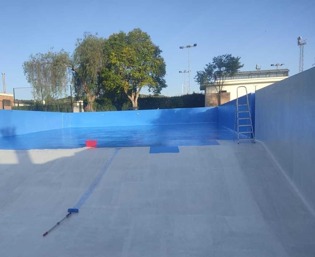 Piscina vacía de hormigón con paredes pintadas de azul y una escalera en el extremo opuesto bajo un cielo despejado.