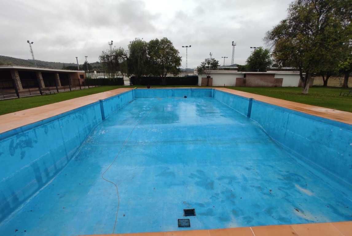 Piscina exterior vacía con suelo azul brillante bajo un cielo nublado.