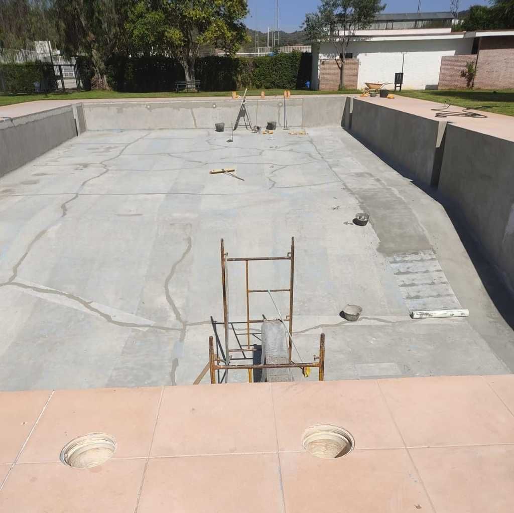 Piscina vacía y desaguada con paredes de hormigón y una escalera bajo la luz del sol.