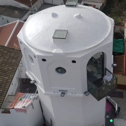 Torre octogonal blanca con techo de tejado con claraboya y ventana redonda, vista desde arriba en un barrio urbano.