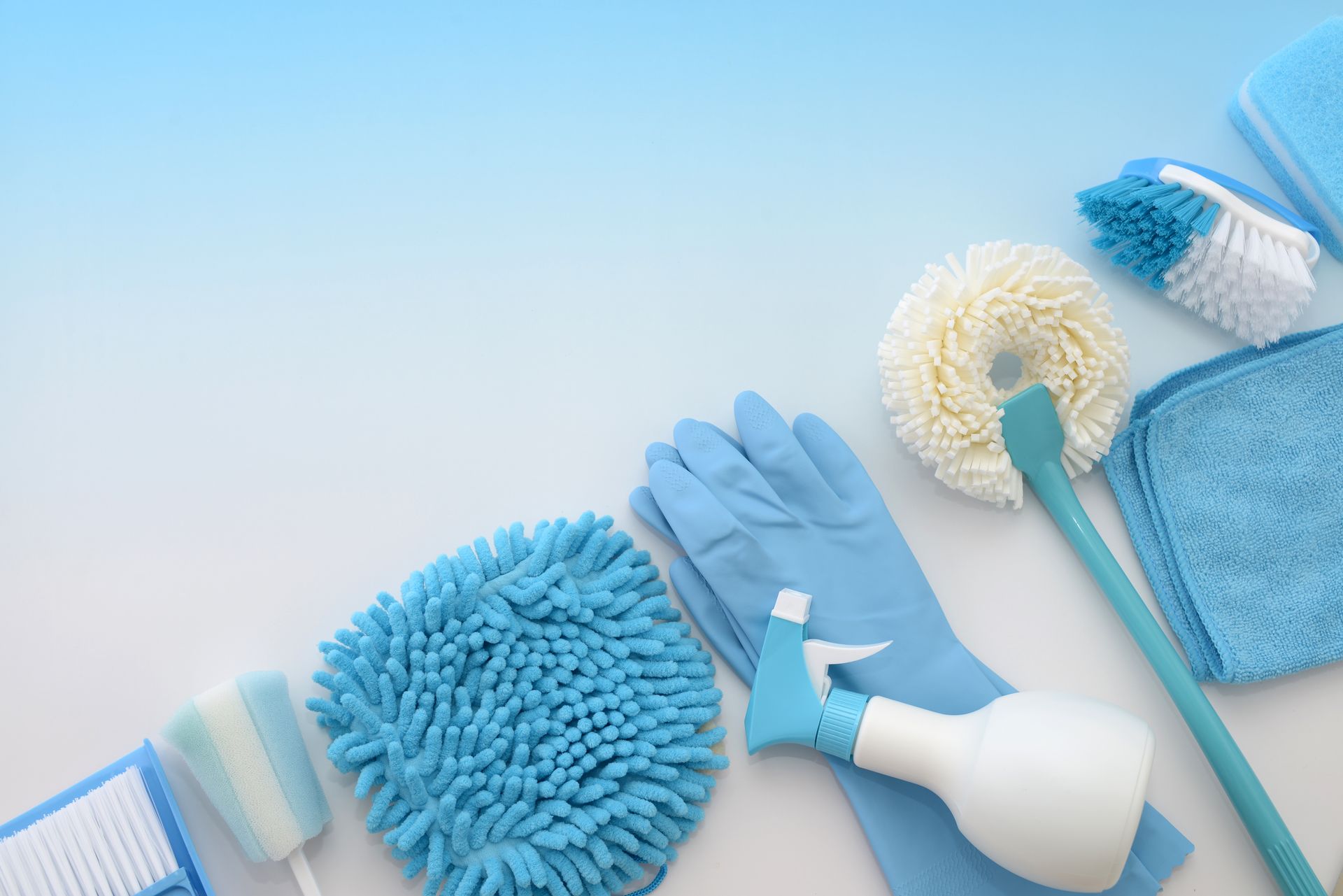 Un assortiment de produits de nettoyage bleus et blancs, comprenant des gants, un flacon pulvérisateur, des brosses et des éponges, sur une surface blanche.